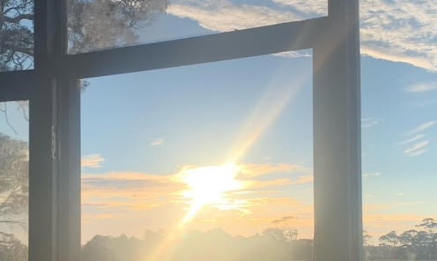 Sunrise seen through a window frame across an open paddock, the sun low over a treeline.